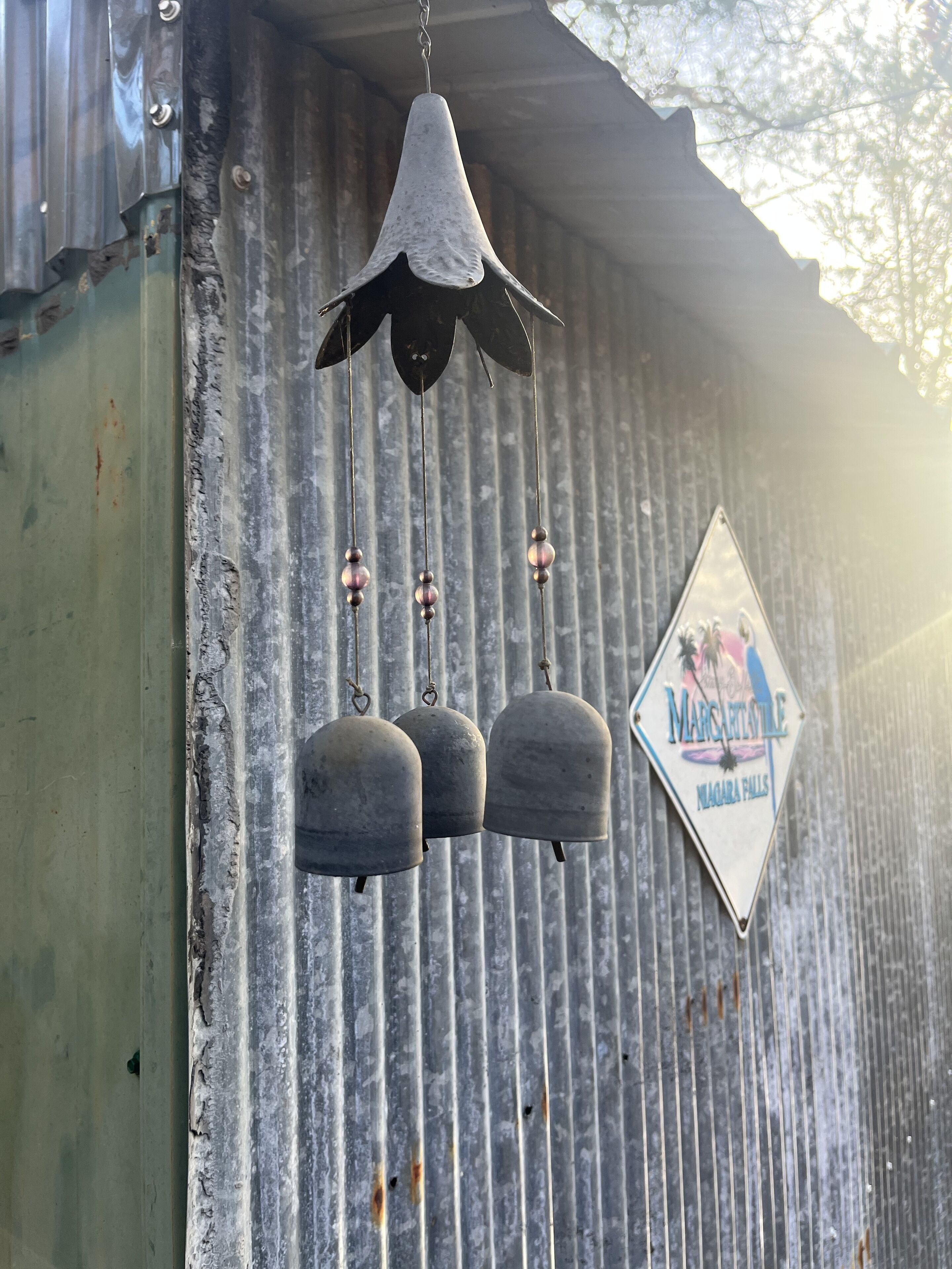Una pared de metal corrugado con una campana colgante y un letrero con forma de diamante.