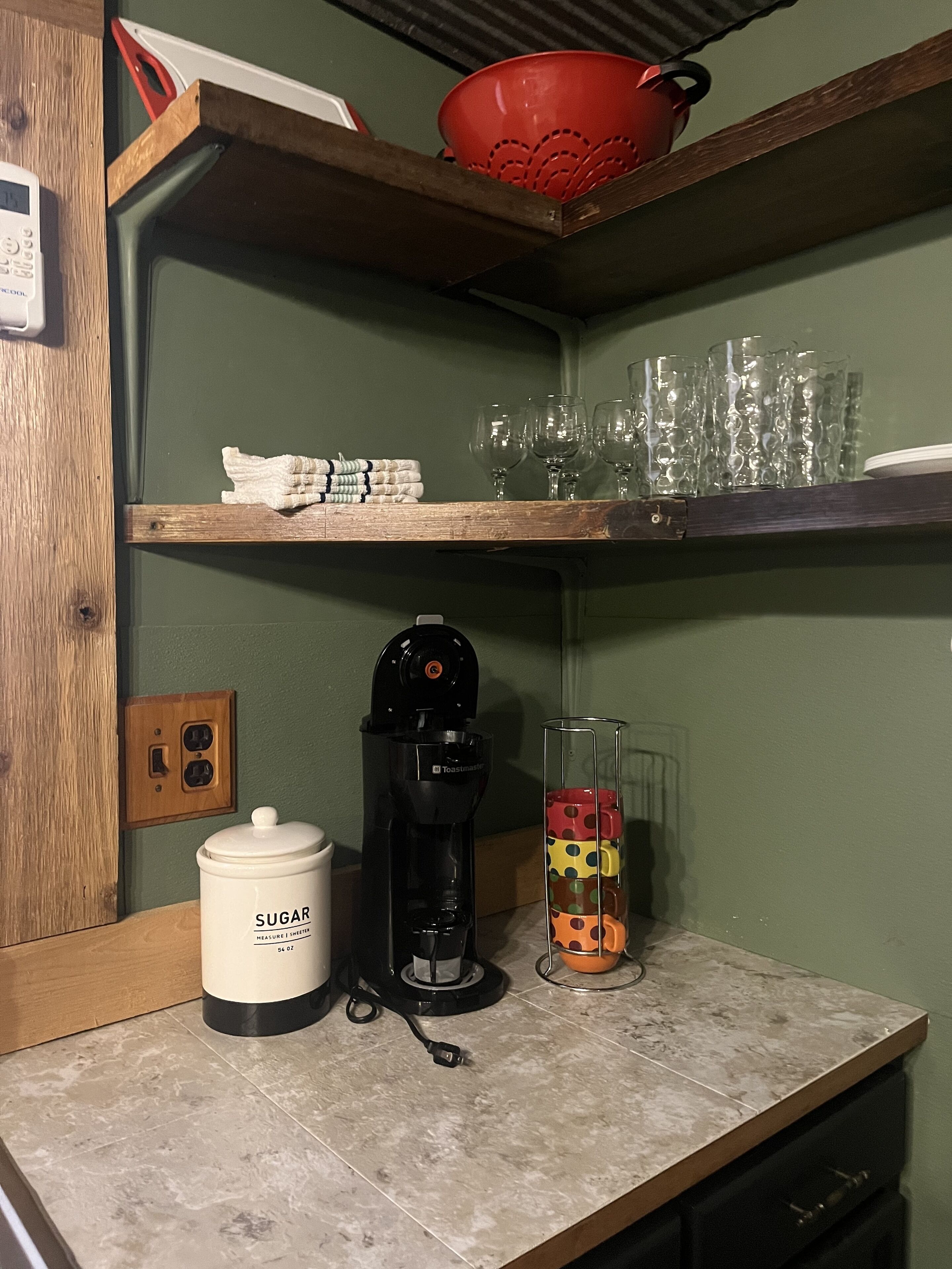 En köksbänk med en kaffebryggare, en sockerskål och en glasbehållare med färgglada lock.