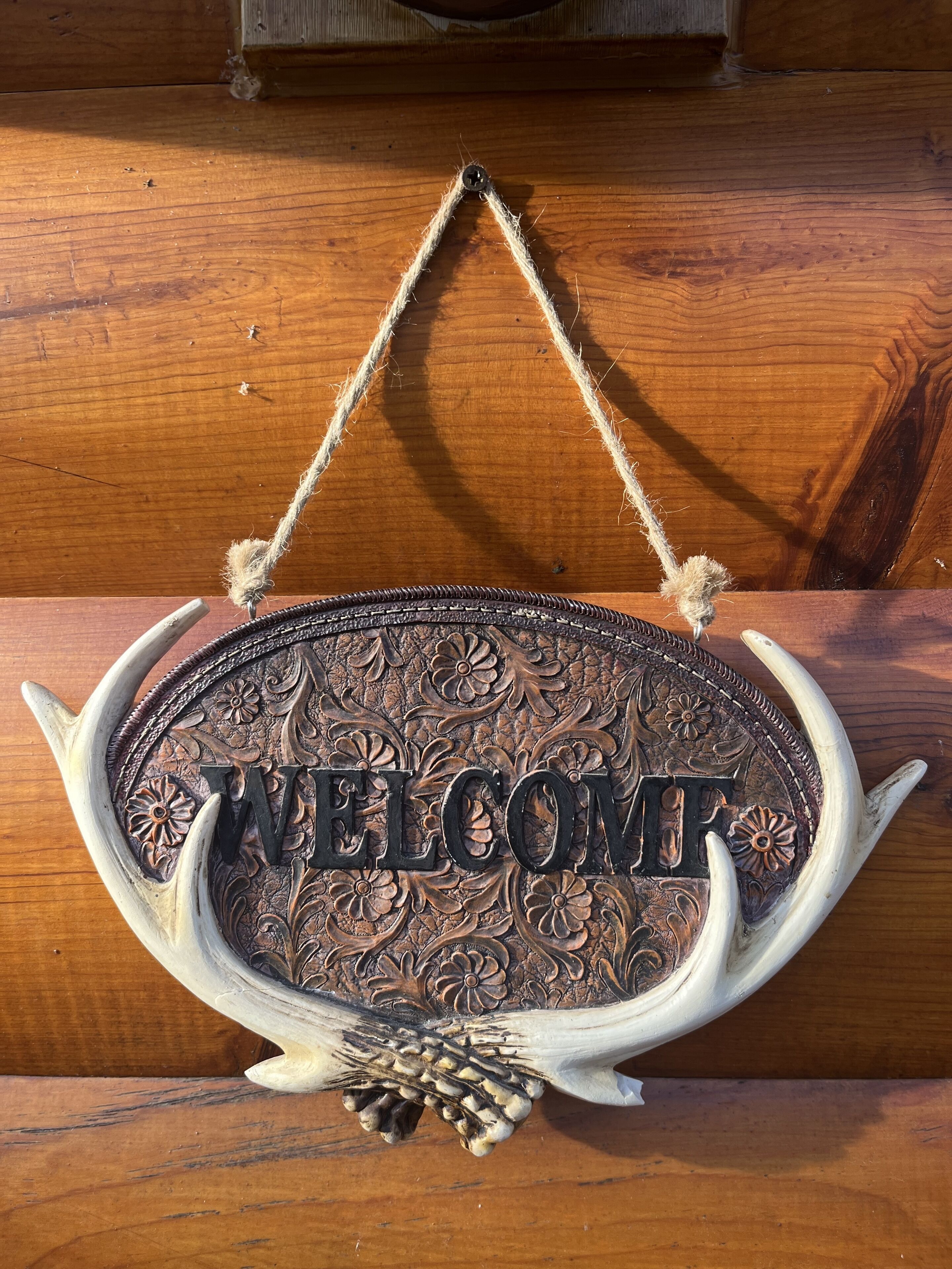 Ein Willkommensschild mit aufwendigen floralen Mustern und dem Wort "WELCOME" in der Mitte, auf einer Holzfläche angebracht.