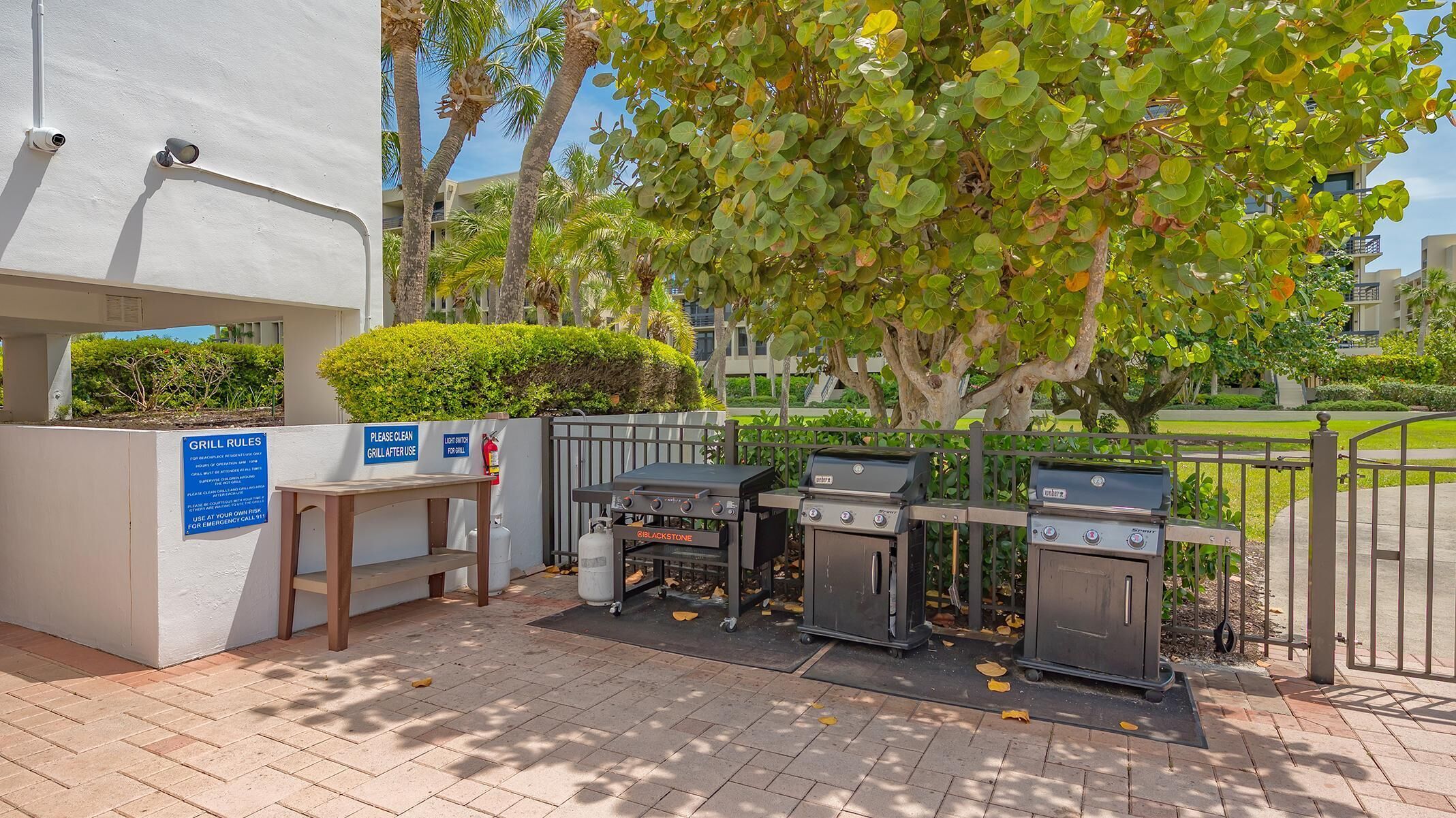 An outdoor barbecue area with grills, a table, and a sign with grill rules.
