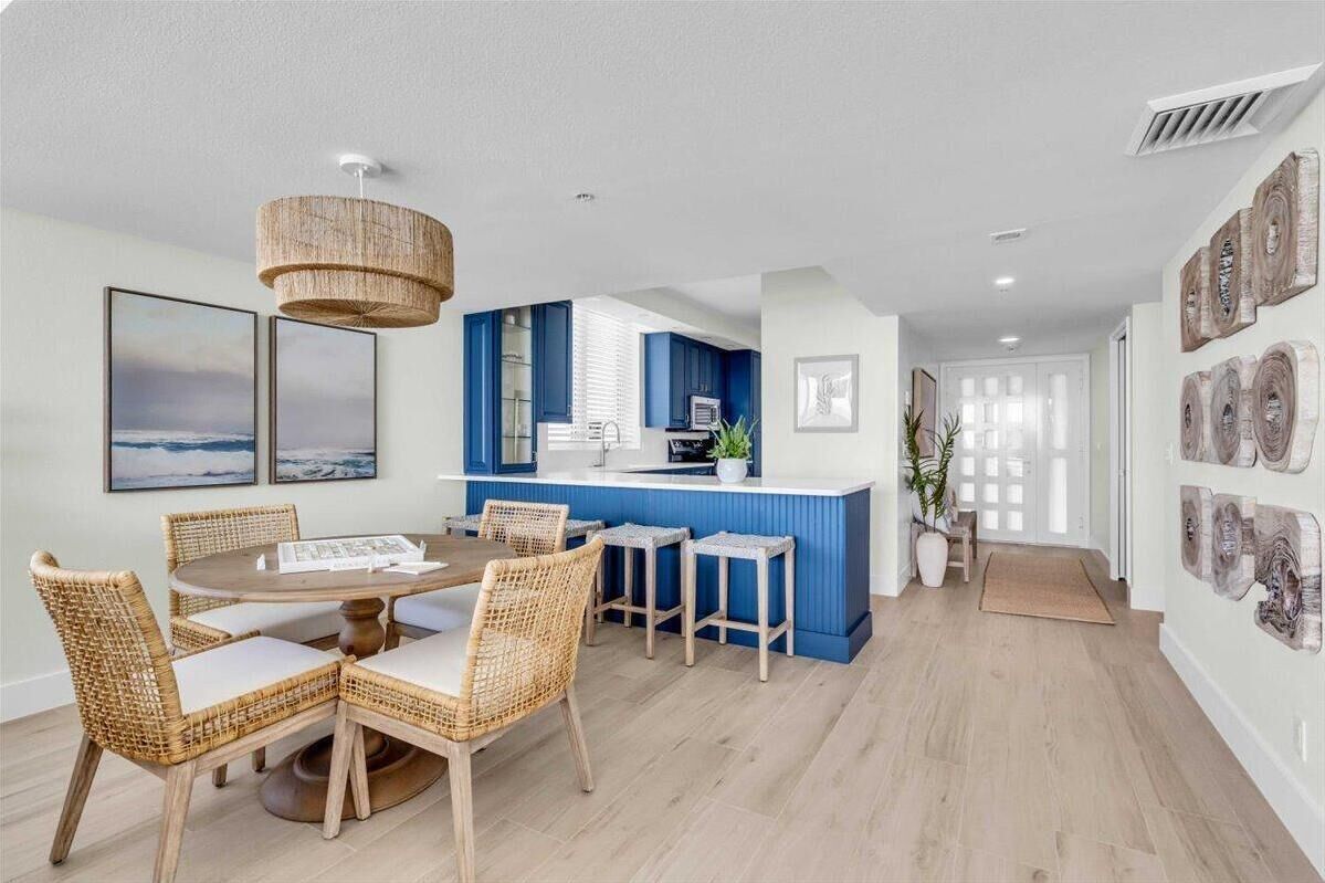 A modern kitchen with blue cabinets, a central island, and a dining area with wicker chairs and a round table.