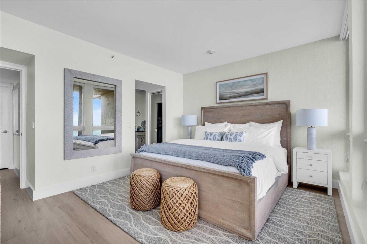 A bedroom with a wooden bed, two bedside lamps, a mirror, and a view of the hallway.