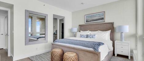 A bedroom with a wooden bed, two bedside lamps, a mirror, and a view of the hallway.