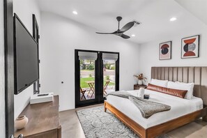 A modern bedroom with a bed, a flat-screen TV, a ceiling fan, and a view of the outdoors through a sliding door.