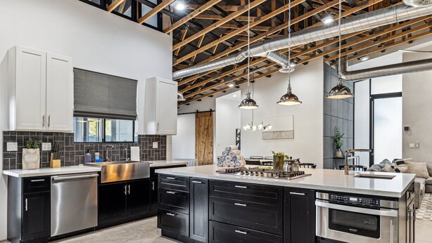 Une cuisine moderne avec des meubles de rangement noirs et blancs, des appareils électroménagers en acier inoxydable et des luminaires suspendus.