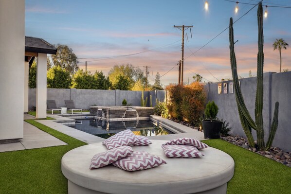 A modern outdoor pool area with artificial lighting, a seating area with cushions, and cacti.