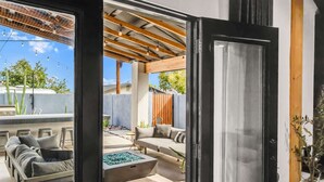 Un patio ouvert avec un espace salon agrémenté de coussins, un foyer et une pergola en bois.