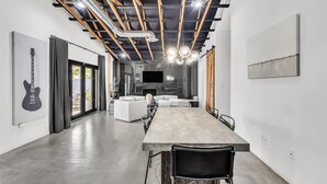 Un intérieur moderne avec une longue table à manger, des canapés blancs et une guitare accrochée au mur.