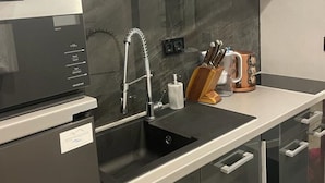 Una cocina moderna con un refrigerador negro, electrodomésticos de acero inoxidable, una encimera negra y un respingo de vidrio.