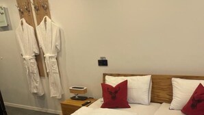 Habitación de hotel con dos camas, una manta roja, toallas blancas, un cabecero de madera y un calentador de pared.