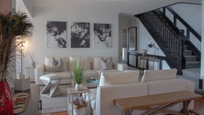 Een moderne woonkamer met een witte zithoek, een houten salontafel en een trap met een zwarre leuning.