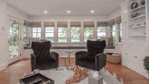 Een woonkamer met twee fauteuils, een bijzettafeltje, een rug met luipaardprint en een vensterbank met uitzicht op een wateroppervlak.