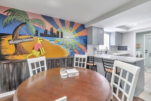 Una cocina moderna con armarios blancos, encimera blanca y un lavabo. En la pared, un mural representa una playa con una palmera y un sol.
