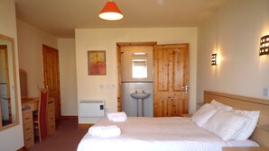Un dormitorio con cama de madera, una mesita de noche, un tocador, un espejo, un aparador, un lavabo y una puerta.