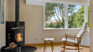 Una habitación con un estufa de leña, un sillón mecedor y una ventana con vistas a los árboles.