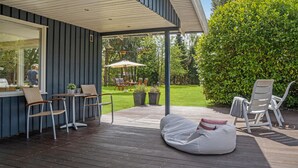 Una terraza con mobiliario exterior, un área de estar cubierta y vistas a un jardín.