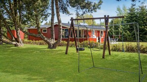 Una cabaña roja con un columpio en un patio cubierto de césped.