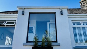 Fachada de um edifício moderno com uma grande janela, um pequeno vaso com plantas e um relógio à esquerda.