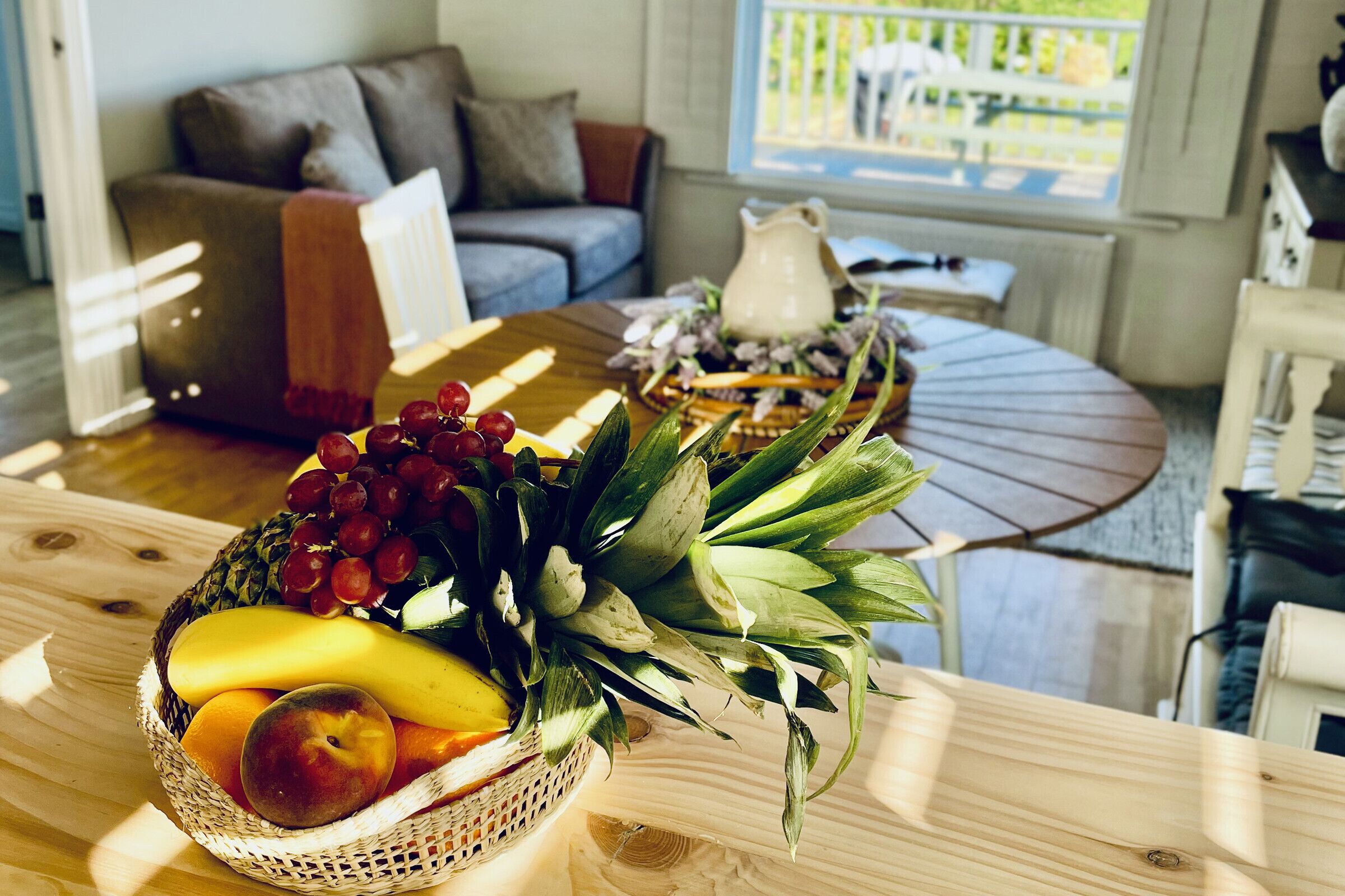 Una mesa de comedor con una cesta de fruta y una jarra.