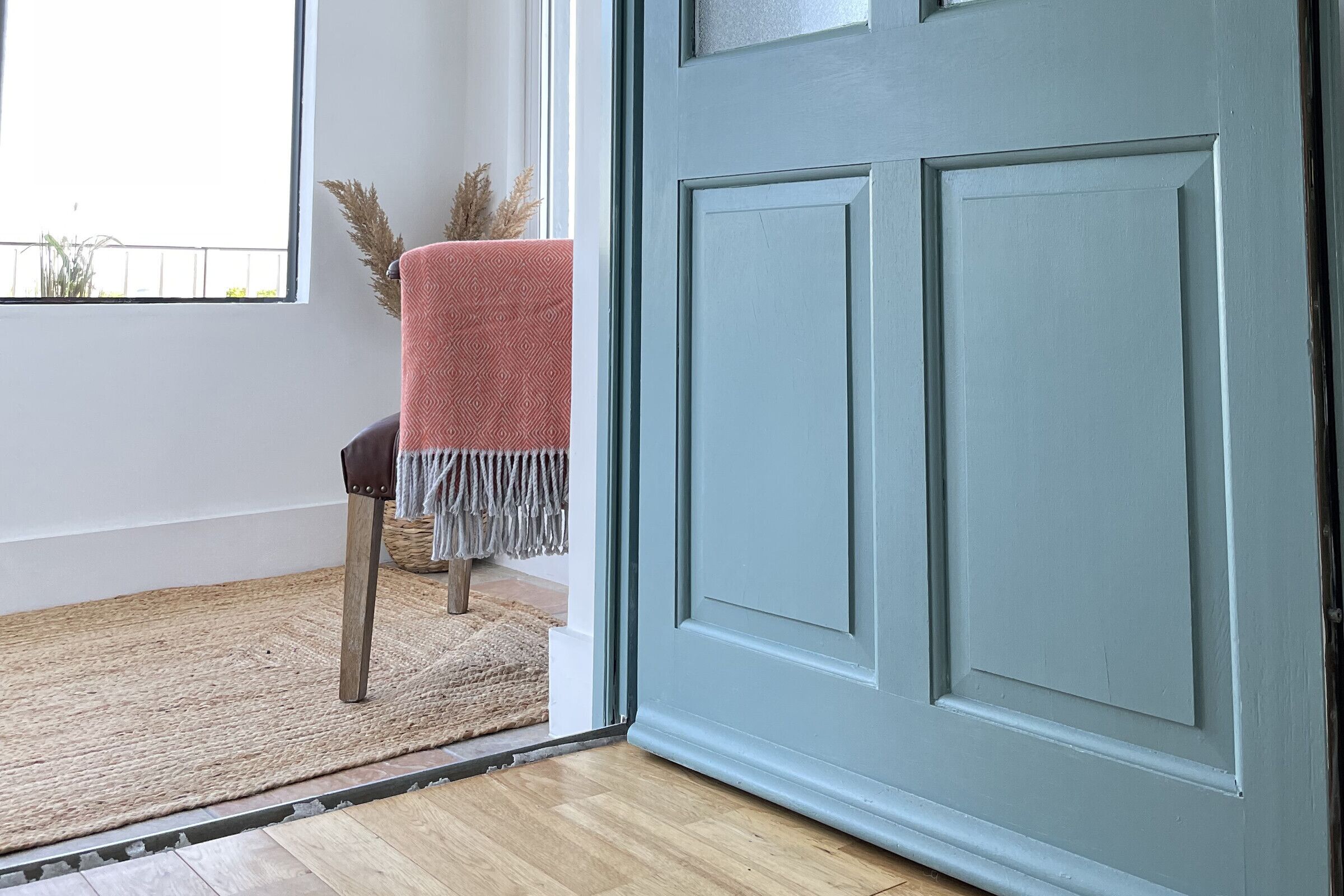 A wooden floor, a grey door, a chair with a red blanket, and a woven mat.