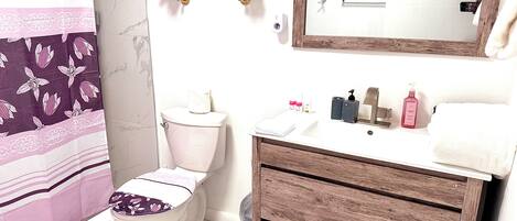 Une salle de bain comprenant des toilettes, un lavabo, un miroir et un espace douche.