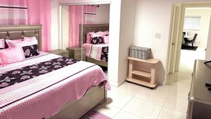 Een slaapkamer met een bed, nachtkastje, dressoir, spiegel en een klein houten plankje.