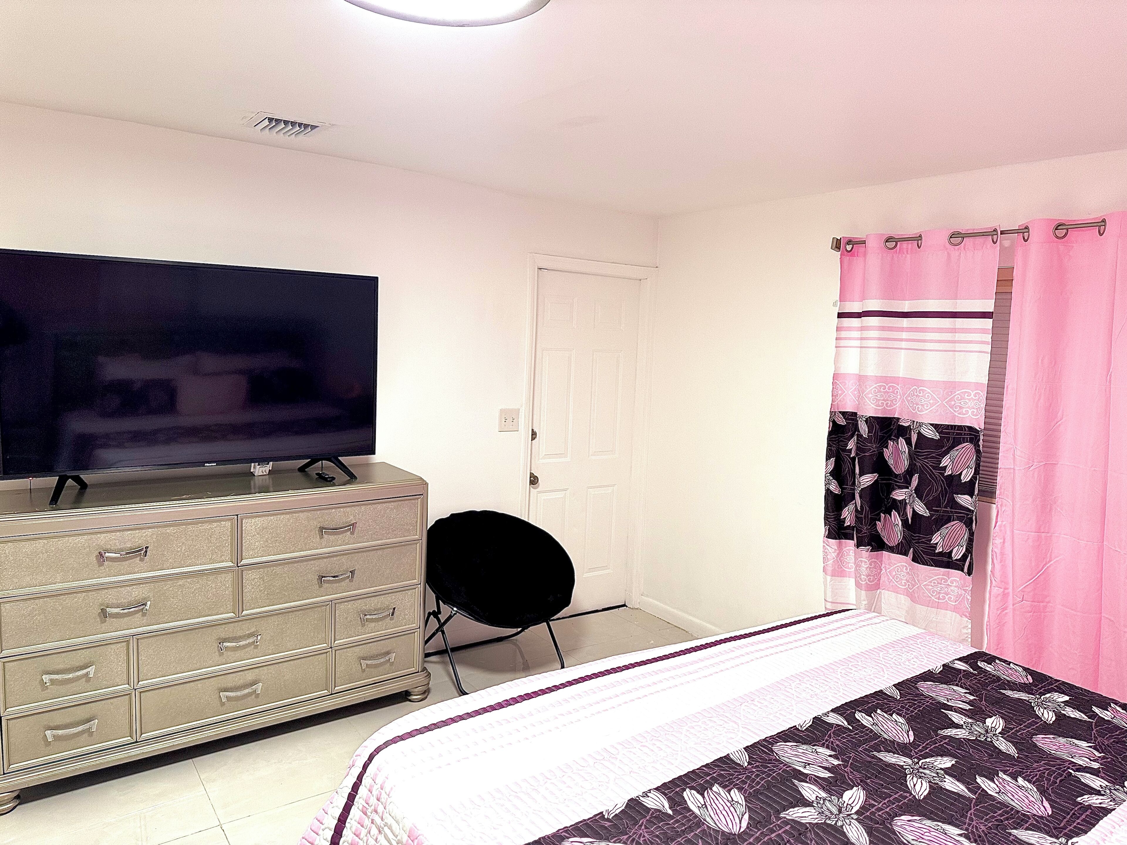 A bedroom with a bed, a dresser, a television on top, and a door.