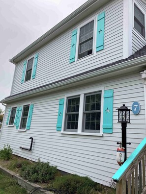 Une maison à deux étages avec des volets turquoise, un numéro « 7 » bien visible et un lampadaire noir.
