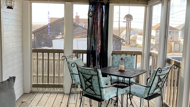 Un patio techado al aire libre con piso de madera, una mesa con sillas y vista al vecindario.