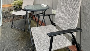 Un patio al aire libre con una mesa y dos sillas, una valla de madera y una ventana con persianas.