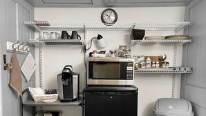 Una kitchenette compacta con microondas, cafetera y estantes para almacenamiento.