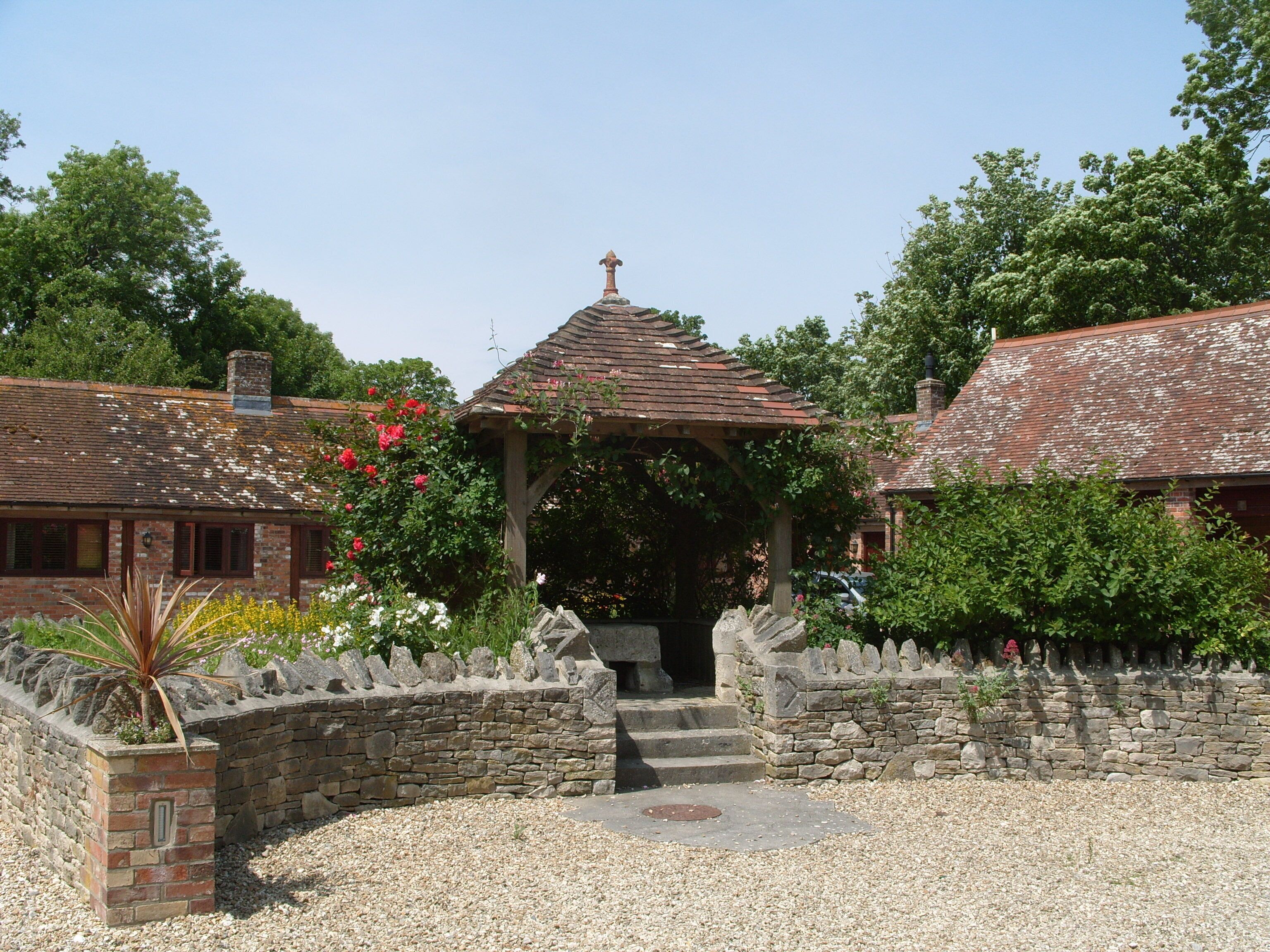 A traditional stone building with a brick facade, a wooden gazebo, and a gravel pathway.