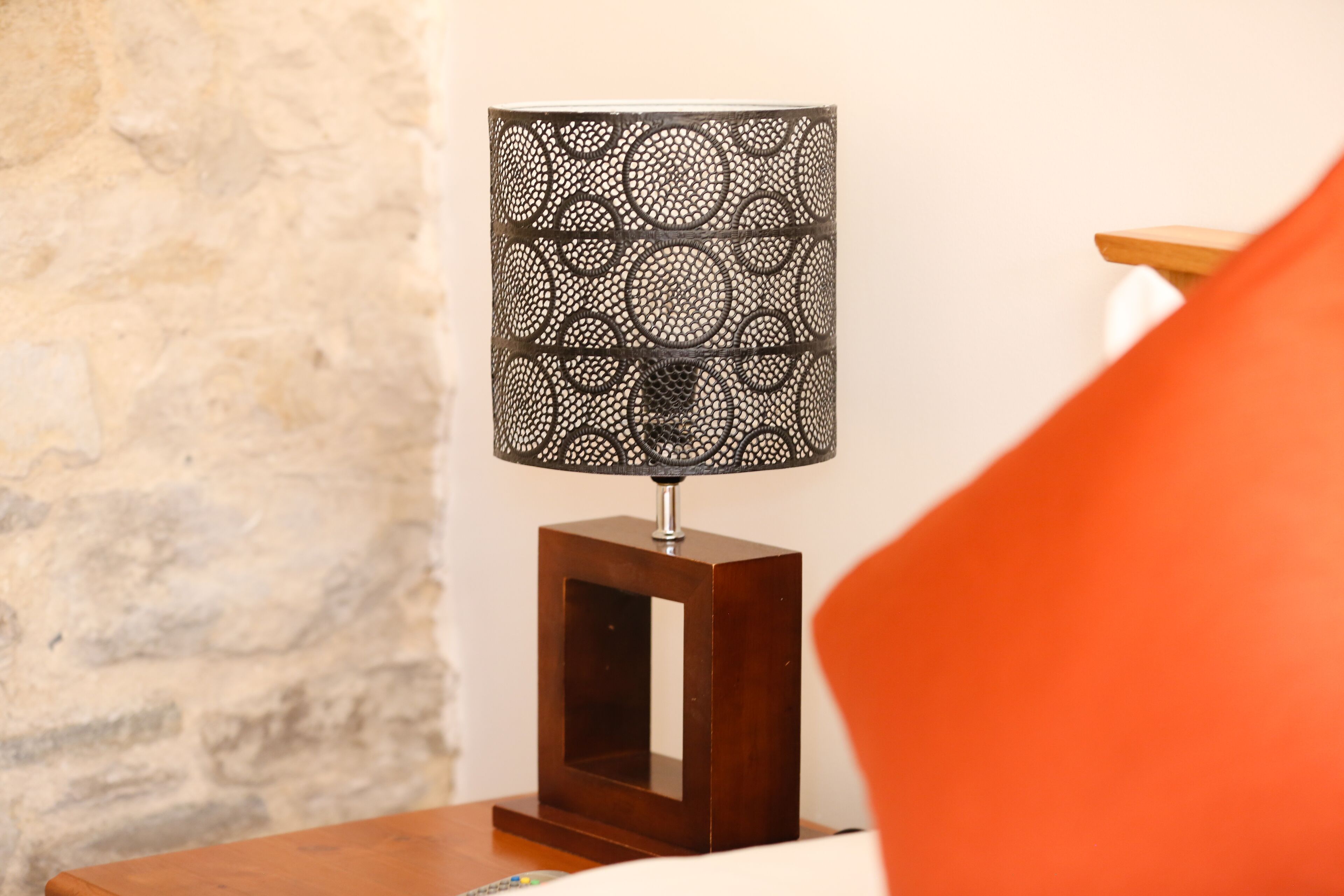 A wooden bedside table with a square mirror and a decorative lamp with a circular pattern.