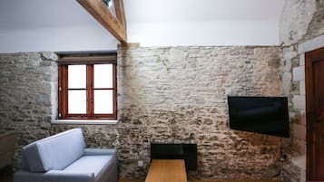 Una stanza con parete in pietra, travi a vista in legno, una finestra, una TV a schermo piatto, un divano e un tavolino.