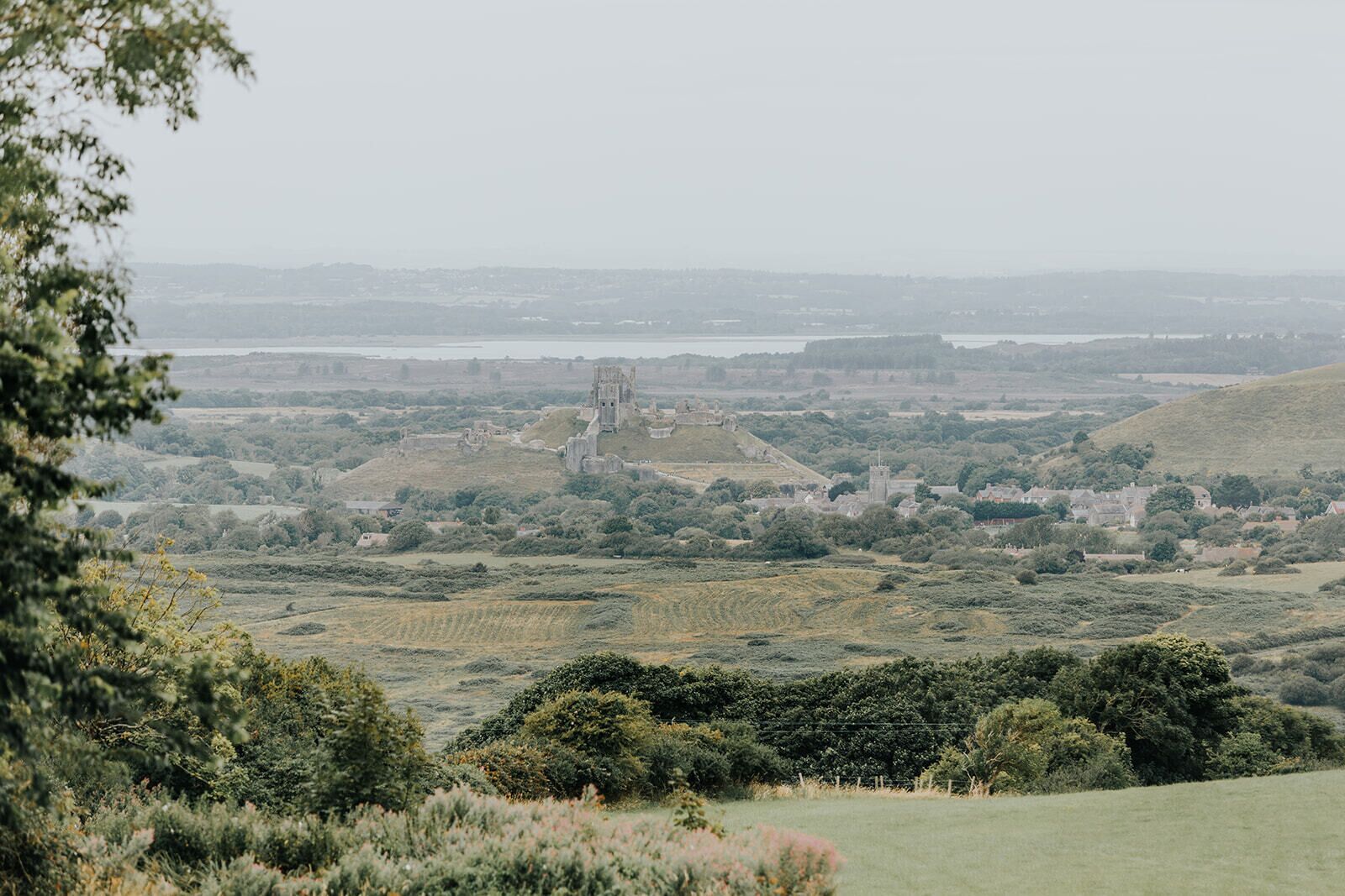 A rural landscape with a prominent stone structure, possibly a ruin, surrounded by fields and trees.