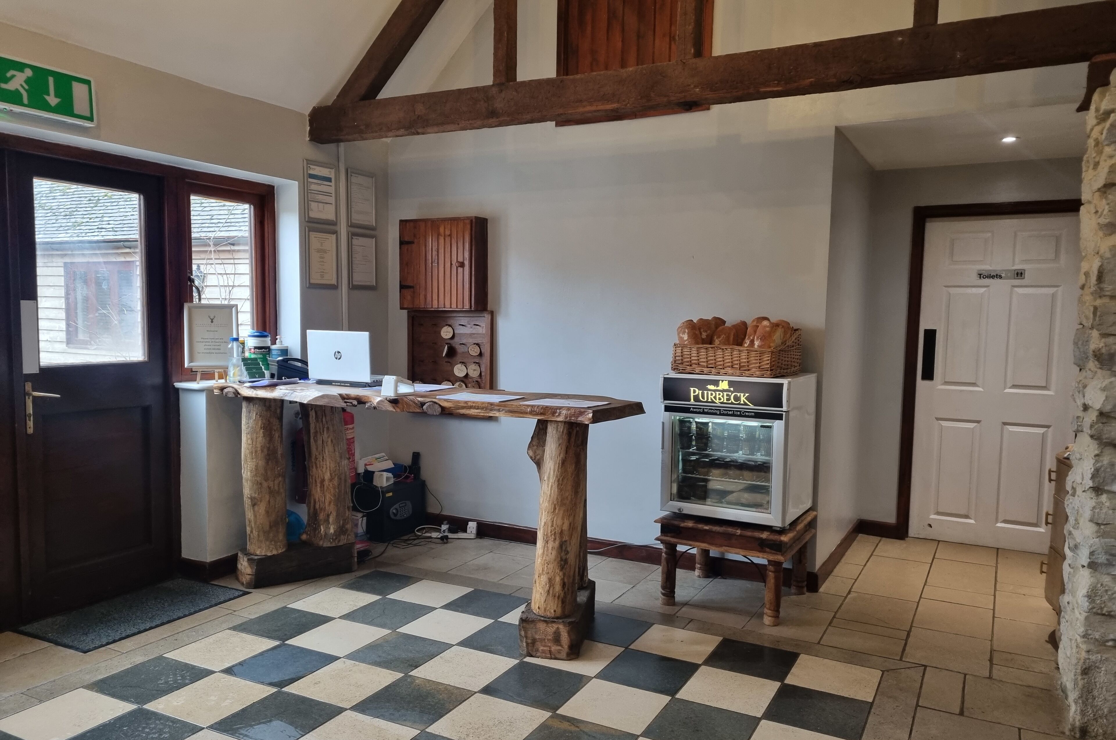 A checkered floor, a wooden table, a small refrigerator, and a door labeled "Toilets".