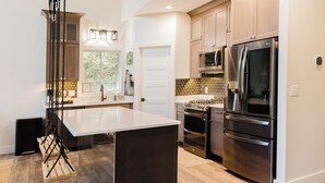 A modern kitchen with stainless steel appliances, a large island, and wooden flooring. - Private Lakehouse getaway with all modern comforts (West Baden Springs)