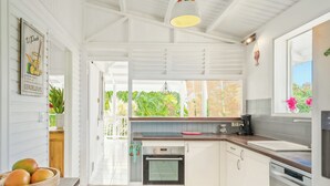 A modern kitchen with white cabinets, a built-in oven, and a window overlooking a garden. - Villa Douce, beach access by foot and private pool (Saint-François)