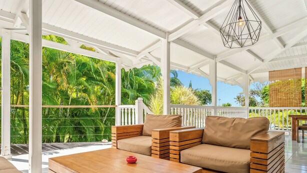 A covered outdoor seating area with wooden furniture and a view of lush greenery. - Villa Douce, beach access by foot and private pool (Saint-François)