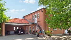 Un bâtiment en briques de deux étages, avec un toit recouvert de tuiles rouges, un espace de stationnement couvert et des places assises à l’extérieur.