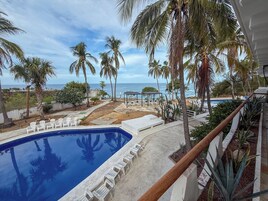 Un área de piscina con sillones de descanso, palmeras y vista al océano.