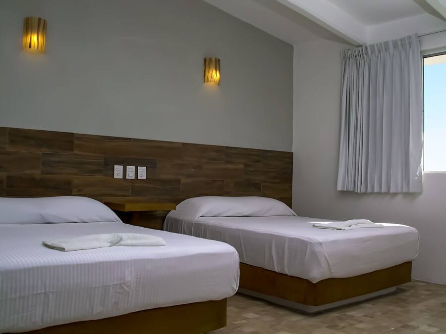 A hotel room with two beds, a wooden headboard, a window with curtains, and wall-mounted lights.