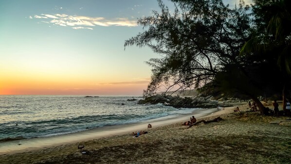 Una playa con gente relajándose, un atardecer y una costa rocosa.