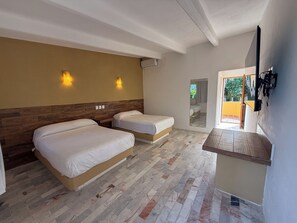 Habitación de hotel con dos camas, cabecero de madera, una mesita pequeña y un espejo.