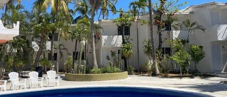 Una piscina con sillas blancas, rodeada de palmeras y un edificio de fachada blanca.