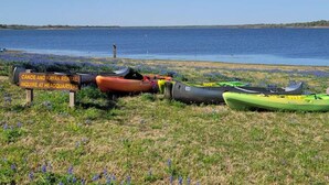 Une zone herbeuse où sont alignés des canoës et des kayaks, un panneau indiquant un service de location de canoës et de kayaks, et une étendue d'eau en arrière-plan.