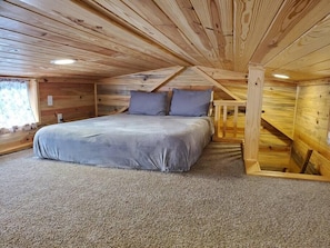 A bedroom with a bed, pillows, carpet, wooden walls, and a window.
