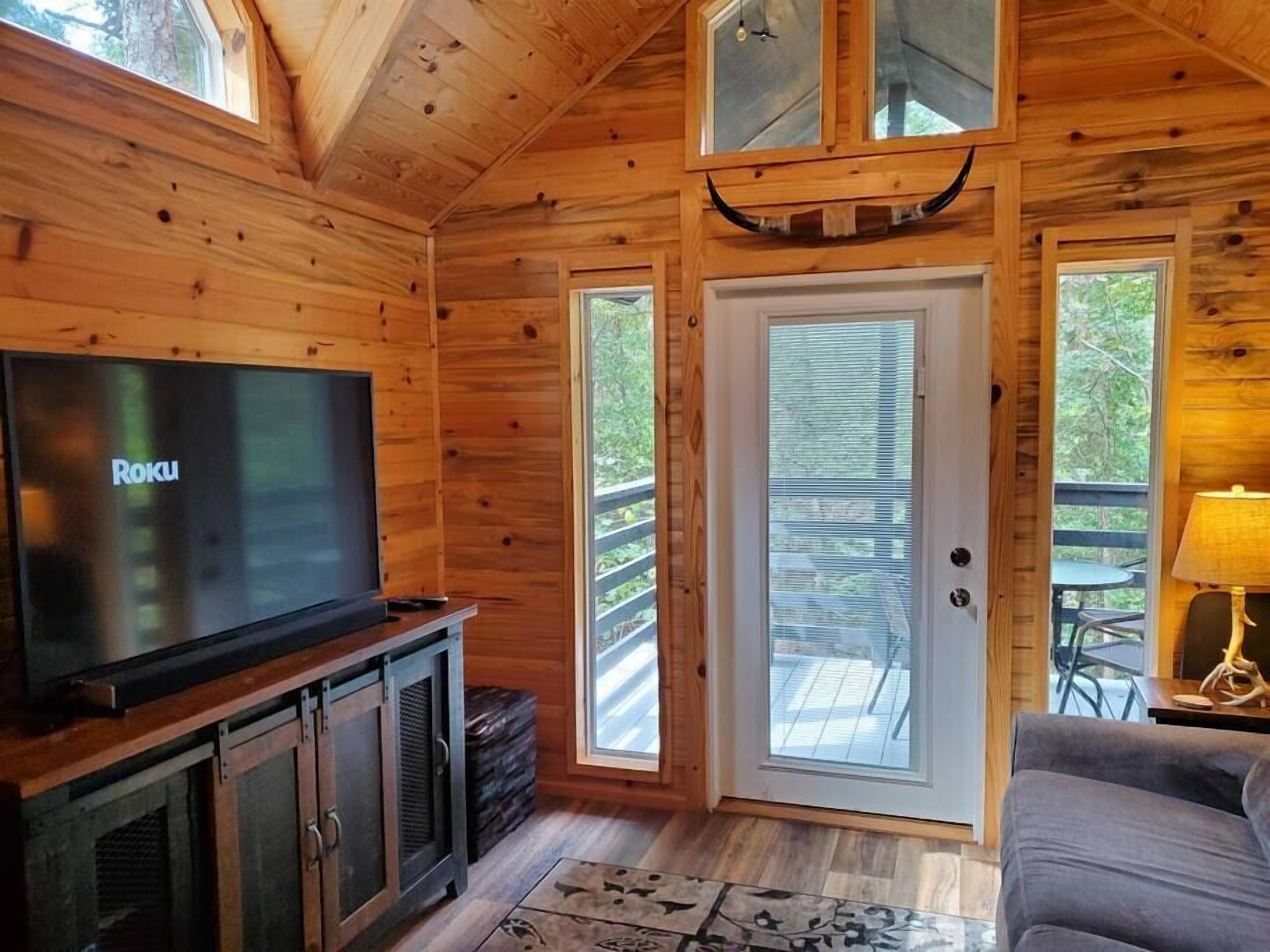 Interior d'una cabana de fusta amb televisió, una porta que dona a l'exterior i una taula petita amb una làmpada.