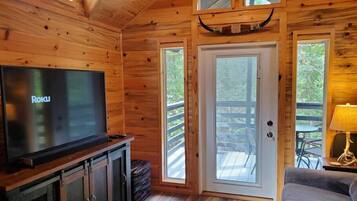 Interior d'una cabana de fusta amb televisió, una porta que dona a l'exterior i una taula petita amb una làmpada.