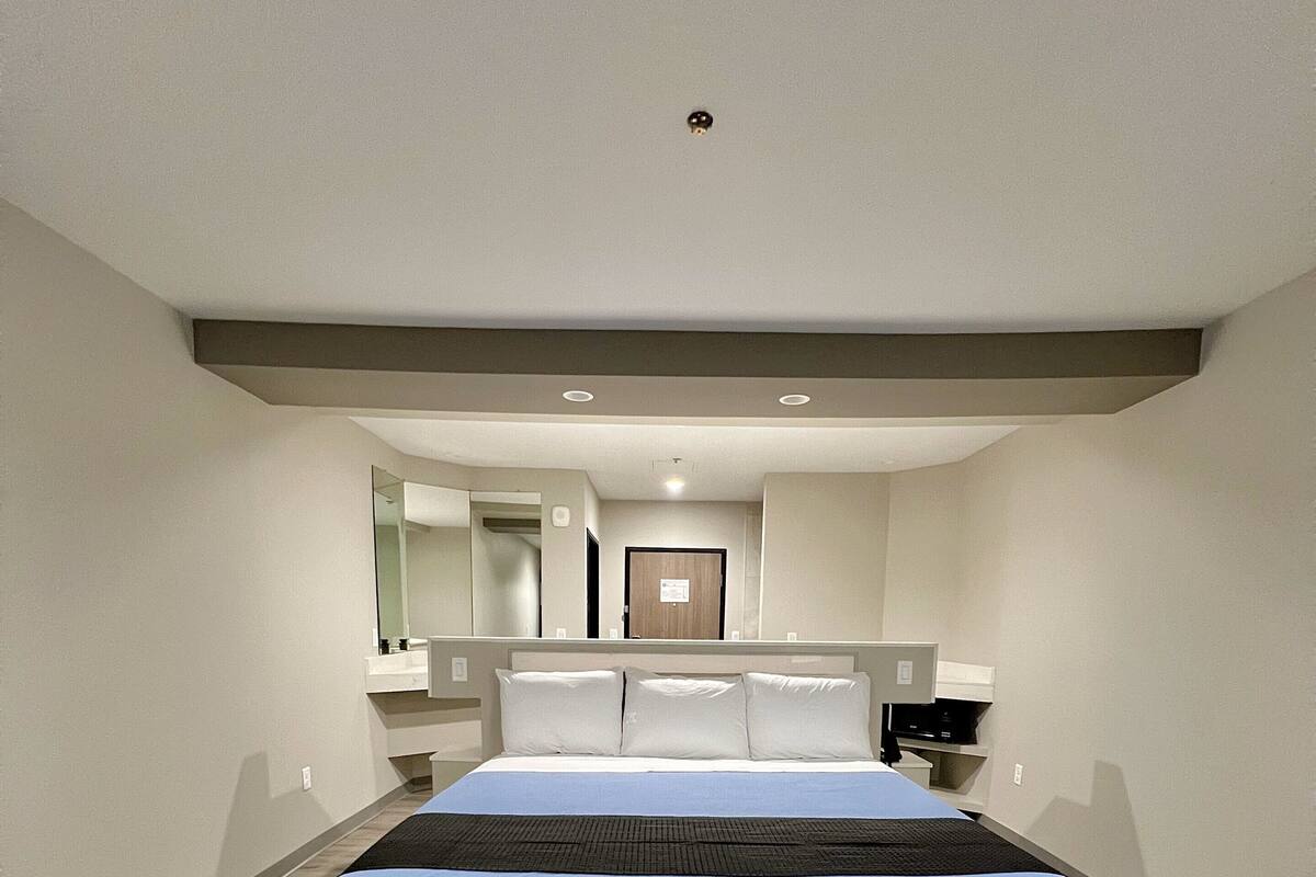 A modern hotel room with a large bed, a desk, a chair, and a mirror.